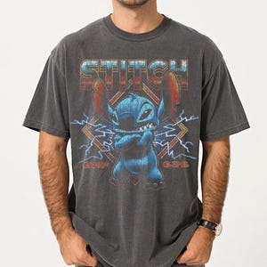 Peut inclure: T-shirt gris fonc&eacute; avec un graphisme du personnage Stitch de Lilo & Stitch. Le motif comprend le mot "Stitch" dans une police r&eacute;tro, Stitch les bras crois&eacute;s et des &eacute;clairs. Le t-shirt est un col rond.