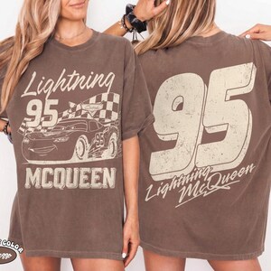 May include: Brown t-shirt featuring a graphic of Lightning McQueen race car with the number 95 and the text "Lightning McQueen". The back of the shirt displays a large number 95 and the text "Lightning McQueen".