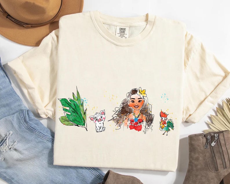 May include: A cream-colored short-sleeve t-shirt featuring a watercolor-style graphic print. The design displays a green tropical leaf, a small pig, a female character with long wavy hair and a flower, and a colorful rooster on the front center.
