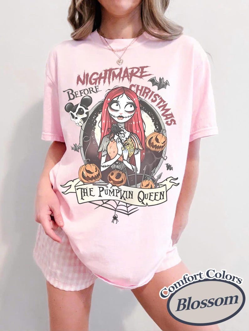 May include: Light pink t-shirt featuring a graphic from "The Nightmare Before Christmas." The design includes Sally, pumpkins, and the text "The Pumpkin Queen." The shirt is labeled "Comfort Colors Blossom."