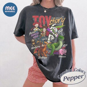 Pu&ograve; includere: Una t-shirt a maniche corte grigio antracite con una stampa grafica dei personaggi di Toy Story, tra cui Jessie, Woody, Buzz Lightyear, Slinky Dog, Bullseye, Rex e Hamm. Il testo riporta Toy Story, Jessie Since 1995, Woody, Buzz, Slinky Dog, Bullseye, Rex e Hamm.