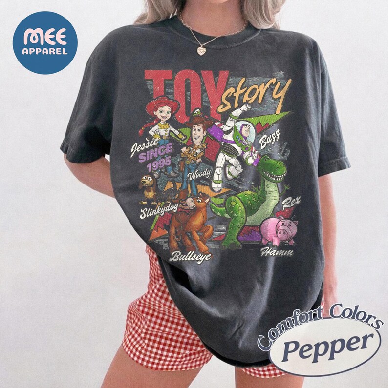 Pu&ograve; includere: Una t-shirt a maniche corte grigio antracite con una stampa grafica dei personaggi di Toy Story, tra cui Jessie, Woody, Buzz Lightyear, Slinky Dog, Bullseye, Rex e Hamm. Il testo riporta Toy Story, Jessie Since 1995, Woody, Buzz, Slinky Dog, Bullseye, Rex e Hamm.