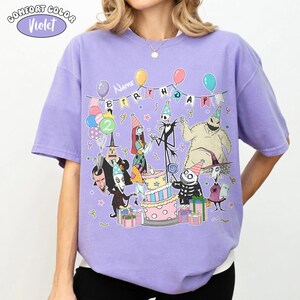 Op de afbeelding: Violet Comfort Colors T-shirt met een kleurrijke afbeelding van personages uit The Nightmare Before Christmas die een verjaardag vieren. Het ontwerp bevat een verjaardagstaart, ballonnen en de tekst "Name Birthday".