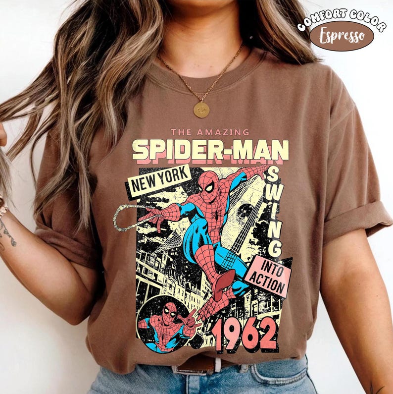 Puede incluir: Una camiseta marr&oacute;n con un gr&aacute;fico de c&oacute;mic de Spider-Man. El dise&ntilde;o incluye el texto "THE AMAZING SPIDER-MAN NEW YORK" y "SWING INTO ACTION 1962". La camiseta es de color Espresso.