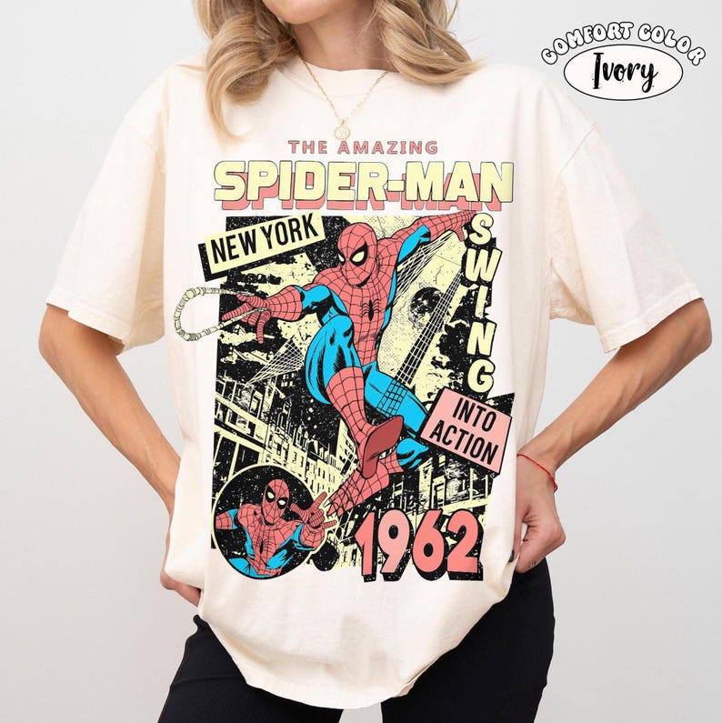 Puede incluir: Camiseta color marfil con un gr&aacute;fico vintage de Spider-Man. El dise&ntilde;o incluye las palabras "THE AMAZING SPIDER-MAN", "NEW YORK" y "1962". Spider-Man se representa con su traje cl&aacute;sico rojo y azul, balance&aacute;ndose. La camiseta est&aacute; etiquetada como "COMFORT COLOR".