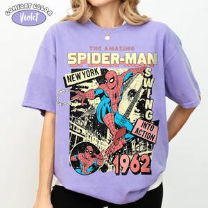 Puede incluir: Una camiseta violeta Comfort Colors con un gr&aacute;fico de Spider-Man. El dise&ntilde;o incluye el texto "THE AMAZING SPIDER-MAN NEW YORK SWING INTO ACTION 1962". La camiseta tiene un estilo de c&oacute;mic vintage.