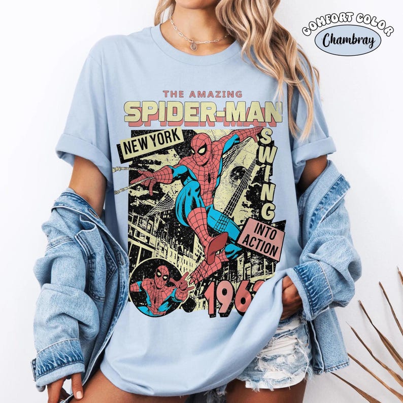 Puede incluir: Camiseta azul claro con un dise&ntilde;o vintage de Spider-Man. El dise&ntilde;o incluye las palabras "The Amazing Spider-Man", "New York" y "Swing Into Action", junto con el a&ntilde;o "1962". El gr&aacute;fico muestra a Spider-Man en acci&oacute;n.