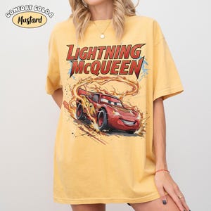 Op de afbeelding: Mosterdkleurig T-shirt met Lightning McQueen uit de film Cars. De afbeelding toont de rode raceauto met vlammen en de tekst "Lightning McQueen" in rood en geel. Het shirt heeft korte mouwen en een relaxte pasvorm.