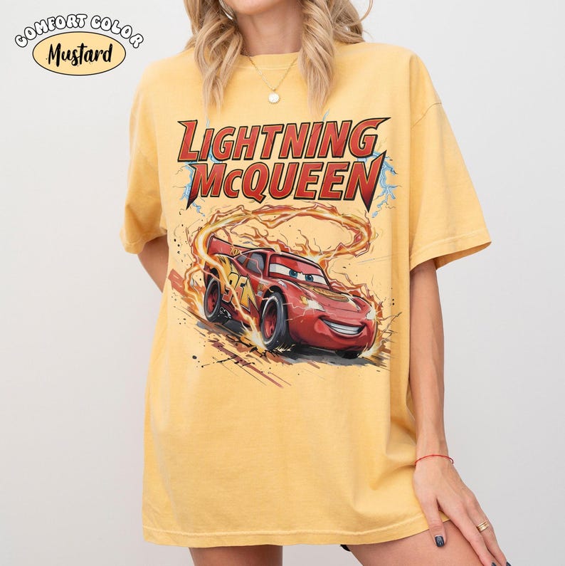 Op de afbeelding: Mosterdkleurig T-shirt met Lightning McQueen uit de film Cars. De afbeelding toont de rode raceauto met vlammen en de tekst "Lightning McQueen" in rood en geel. Het shirt heeft korte mouwen en een relaxte pasvorm.