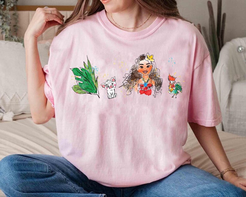May include: A light pink short-sleeve t-shirt featuring a watercolor-style graphic print. The design includes a green tropical leaf, a small white pig, a female character with long brown hair and a yellow flower, and a colorful rooster character.