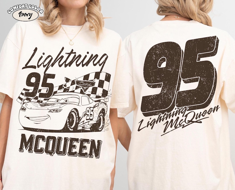 May include: Ivory-colored t-shirt featuring a distressed graphic of Lightning McQueen from the movie Cars. The front displays the text "Lightning 95 McQueen" with an image of the car and a checkered flag. The back has a large "95" and "Lightning McQueen".