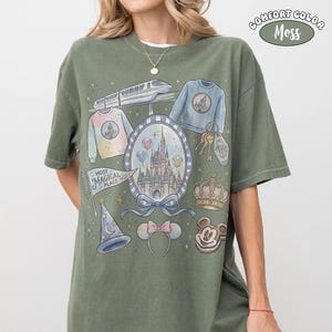 Puede incluir: Camiseta verde oliva Comfort Colors con una ilustraci&oacute;n tem&aacute;tica. El dise&ntilde;o incluye un castillo, Mickey Mouse, una corona y otros elementos. Las palabras "Most Magical Place" est&aacute;n en una pancarta. La camiseta tiene mangas cortas y un corte holgado.