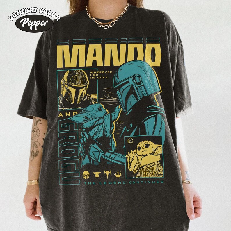 Pode incluir: Camiseta cinza escuro com um design gr&aacute;fico com o texto "MANDO" em letras amarelas. O design inclui ilustra&ccedil;&otilde;es de The Mandalorian e Grogu, com o texto "THE LEGEND CONTINUES". A camiseta tem um visual vintage e desgastado.