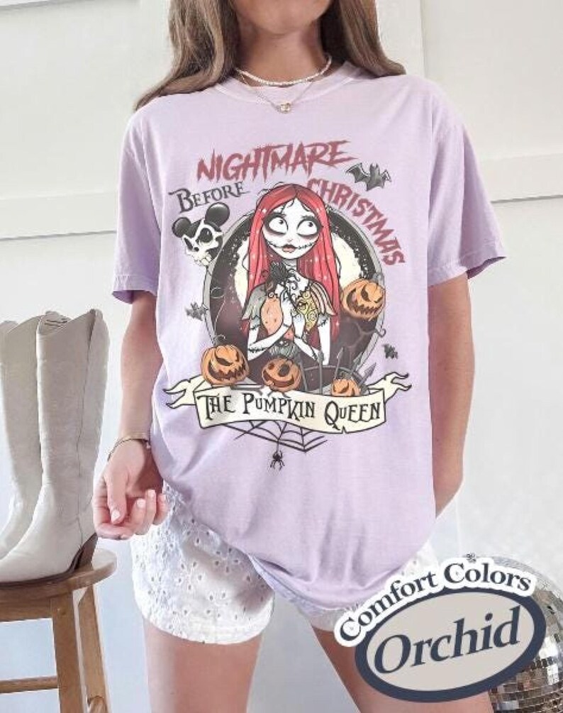 May include: Orchid-colored t-shirt featuring a graphic from "The Nightmare Before Christmas." The design includes Sally, pumpkins, and the text "The Pumpkin Queen." The shirt has short sleeves and a relaxed fit.