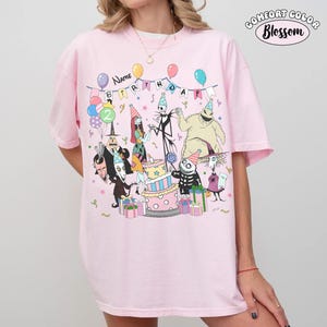 Op de afbeelding: Roze Comfort Colors T-shirt met een verjaardagsfeestje met personages uit The Nightmare Before Christmas. Het ontwerp bevat een taart, ballonnen en de woorden "Name Birthday". Het shirt heeft een relaxte pasvorm.