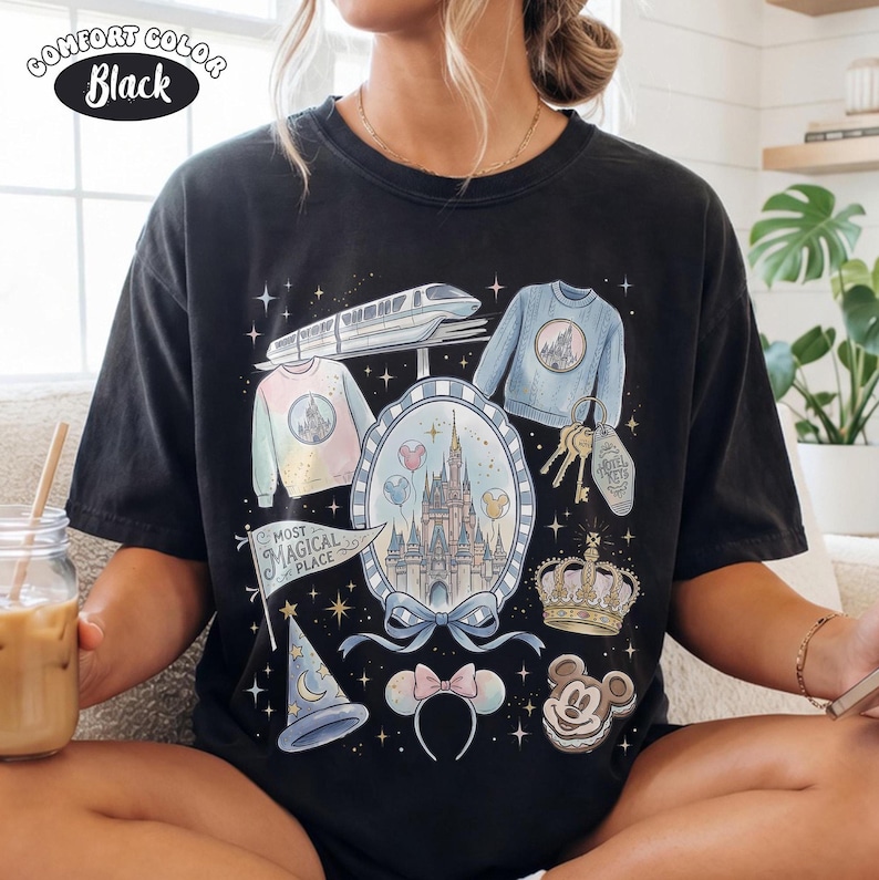 Puede incluir: Camiseta negra Comfort Colors con un gr&aacute;fico colorido de un castillo, su&eacute;teres, un tren y otros elementos tem&aacute;ticos. La camiseta incluye el texto "Most Magical Place" en una bandera y una galleta de Mickey Mouse.