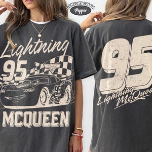 May include: Dark gray t-shirt featuring a graphic of Lightning McQueen from the Cars movie. The front design includes the number 95, the name "Lightning McQueen," and the word "McQueen." The back of the shirt displays a large "95" and "Lightning McQueen."