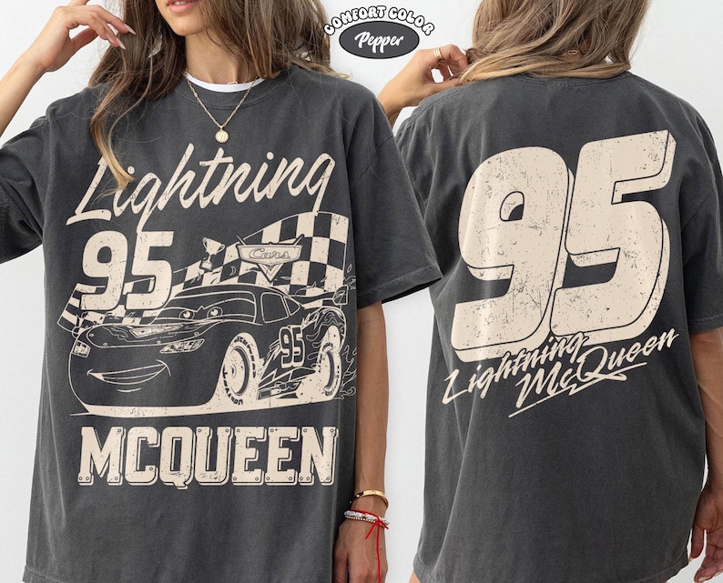 May include: Dark gray t-shirt featuring a graphic of Lightning McQueen from the Cars movie. The front design includes the number 95, the name "Lightning McQueen," and the word "McQueen." The back of the shirt displays a large "95" and "Lightning McQueen."