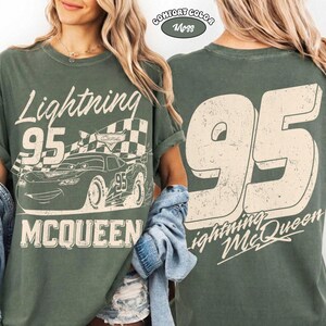 May include: A green t-shirt featuring Lightning McQueen from the Cars movie. The front graphic includes the text "Lightning 95 McQueen" with a checkered flag and a cartoon car. The back of the shirt displays a large "95" and "Lightning McQueen".
