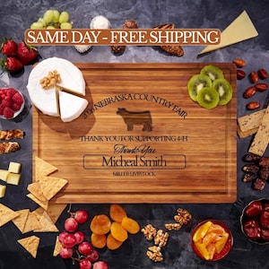 May include: A rectangular bamboo cutting board engraved with the text 2026 NEBRASKA COUNTRY FAIR, THANK YOU FOR SUPPORTING 4-H, Thank You, Micheal Smith, and MILLER LIVESTOCK, featuring a cow silhouette, surrounded by cheese, fruit, and nuts.