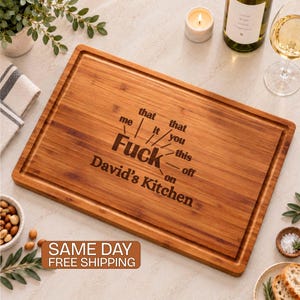 May include: A rectangular bamboo cutting board with a juice groove, laser-engraved with the text 'Fuck' surrounded by radiating words 'me', 'that', 'it', 'that', 'you', 'this', 'off', 'on', and the name 'David’s Kitchen' centered below.