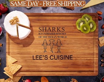 May include: A rectangular bamboo cutting board featuring a laser-engraved design with the text SHARKS ILLUSTRATED SPECIES OF THE OCEAN WORLD, three shark silhouettes, and the text LEE'S CUISINE, surrounded by various food items like cheese and fruit.