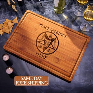 May include: A rectangular bamboo cutting board featuring a laser-engraved design of a goat skull inside a pentagram with the text "PLACE SACRIFICE HERE". The board has a grooved perimeter and a natural wood grain finish with light and dark brown tones.
