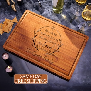 May include: A rectangular wooden cutting board with a juice groove. The board has the text "AS FOR ME AND MY HOUSE WE WILL SERVE the Lord Joshua 24:15 The Clarke Family" engraved on it. The board is surrounded by wine glasses, candles, and snacks.