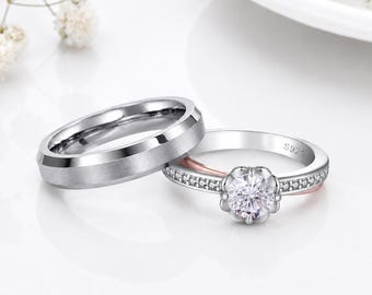 Puede incluir: Una alianza de boda plateada con acabado cepillado junto a un anillo de compromiso plateado con una piedra central redonda, un engaste en forma de flor y pequeñas piedras pavé a lo largo del aro, con el grabado S925 visible en el interior.