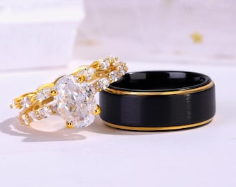 May include: A set of two wedding bands. The woman's ring features a large oval-shaped diamond surrounded by smaller diamonds set in a gold band. The man's ring is a black band with a gold trim.