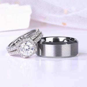 May include: A set of wedding rings, one with a large, round, clear stone surrounded by smaller stones, and the other a simple, silver band.