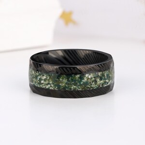 May include: Black ring with a green and white camouflage pattern inlay. The ring has a brushed finish and a beveled edge.