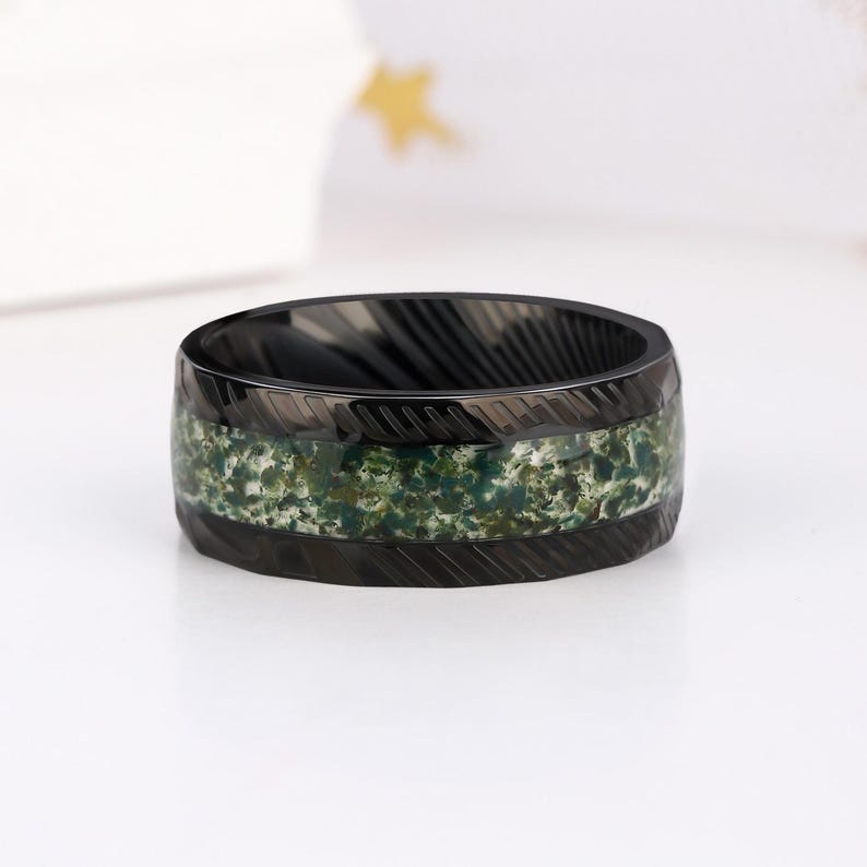 May include: Black ring with a green and white camouflage pattern inlay. The ring has a brushed finish and a beveled edge.