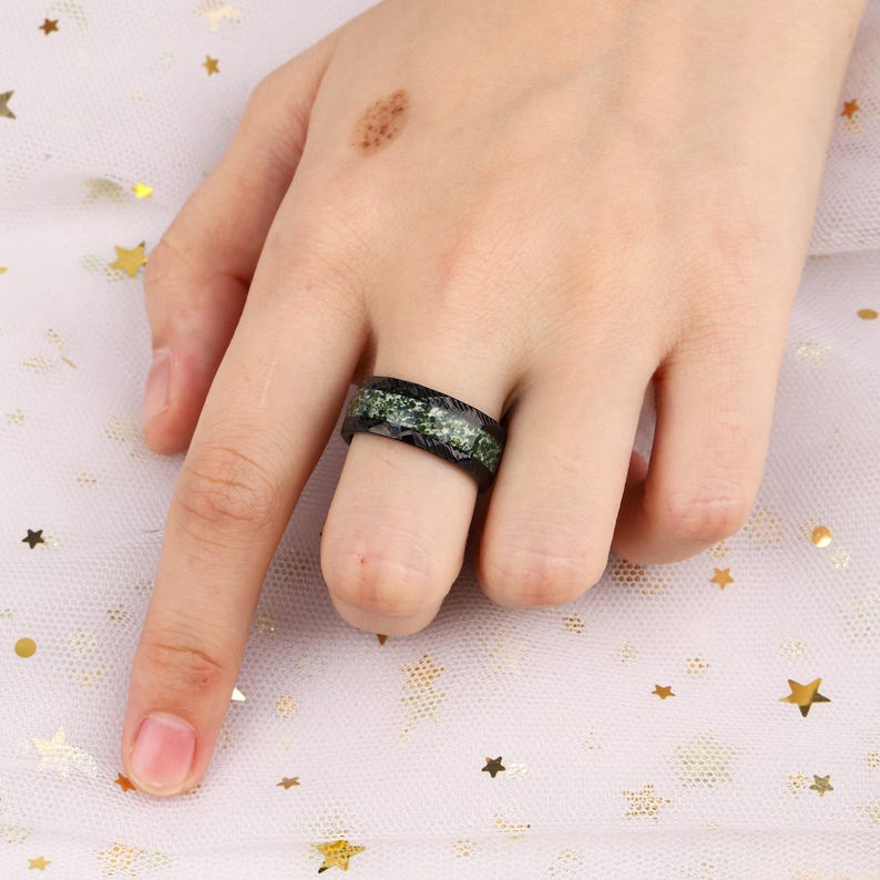 May include: A black ring with a green inlay. The ring is worn on a finger.