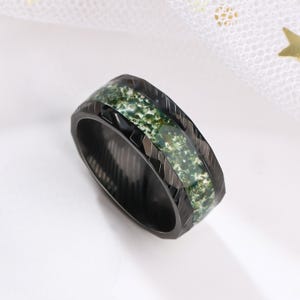 May include: Black ring with a green and black patterned inlay. The ring has a textured, grooved design.