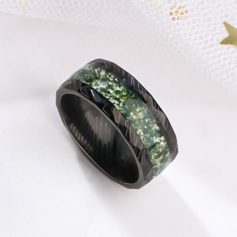 May include: Black ring with a green and black patterned inlay. The ring has a textured, grooved design.