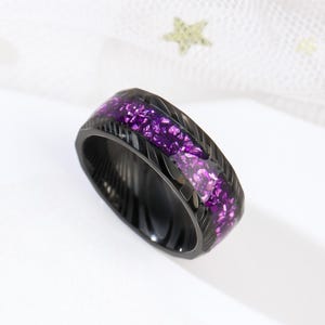 May include: A black ring with a purple glitter inlay. The ring has a textured, brushed finish.