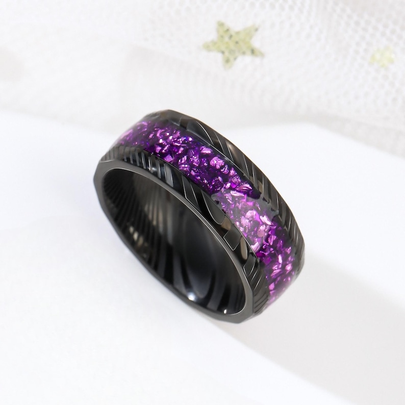 May include: A black ring with a purple glitter inlay. The ring has a textured, brushed finish.