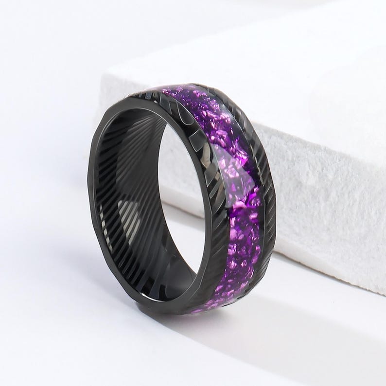 May include: A black ring with a purple glitter inlay. The ring has a textured band and a polished finish.