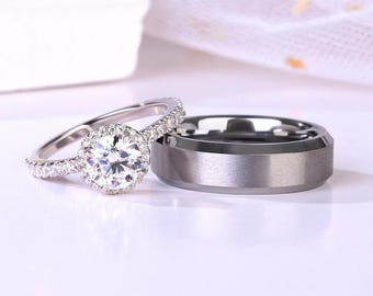 Puede incluir: Un juego de anillos de boda, uno con un gran diamante redondo y claro rodeado de diamantes más pequeños y una banda plateada, y el otro una banda plateada lisa.