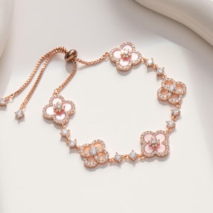 May include: Rose gold bracelet featuring four-leaf clover charms with pink centers and sparkling accents. The bracelet has a delicate chain and adjustable closure, perfect for adding a touch of elegance to any outfit.