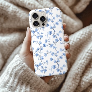 Silicone Phone Case Mockup of an iPhone held by a young woman's hand in front of some cozy beige wool blankets. Works in Photoshop, Photopea and Canva.