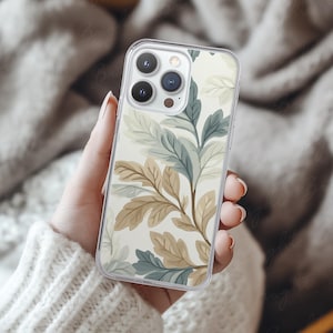 Phone case mockup of a clear phone case held by a girl's hand that's wearing a wool white sweater, in front of a cozy blanket. Works in Photoshop, Photopea and Canva.