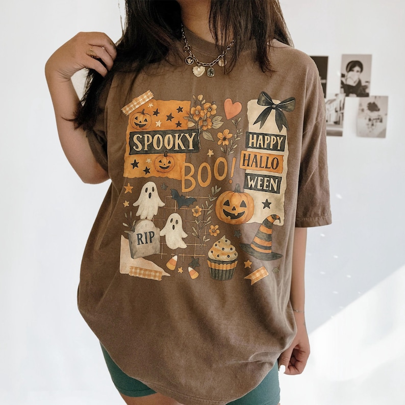 K&ouml;nnte beinhalten: Braunes Halloween-T-Shirt mit einem grafischen Design mit K&uuml;rbissen, Geistern, einem Hexenhut und den Worten "Spooky Boo! Happy Halloween". Das Design umfasst Sterne, Blumen und einen Cupcake.