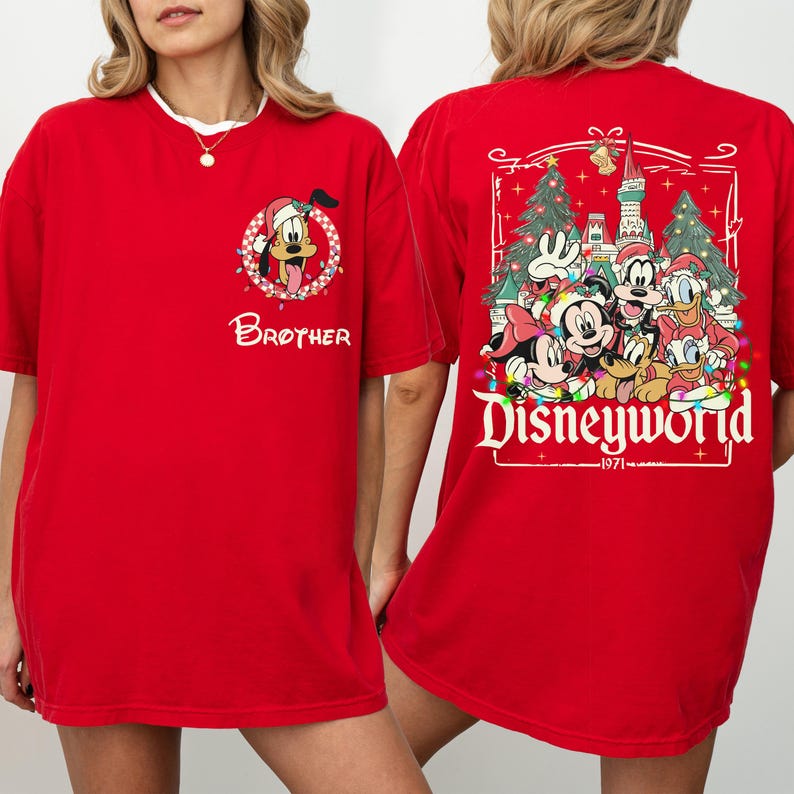 May include: Red t-shirt featuring a cartoon of Pluto wearing a Santa hat and the word "Brother". The back of the shirt displays Disney characters in front of a castle and Christmas trees, with the text "Disneyworld - 1971".