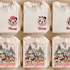 K&ouml;nnte beinhalten: Off-white T-Shirts mit Disney-Charaktergrafiken. Ein Shirt zeigt Minnie Mouse mit dem Wort "Mommy", ein anderes Mickey Mouse mit "Daddy" und ein drittes Pluto mit "Brother". Andere Shirts zeigen eine Disneyland-Grafik.