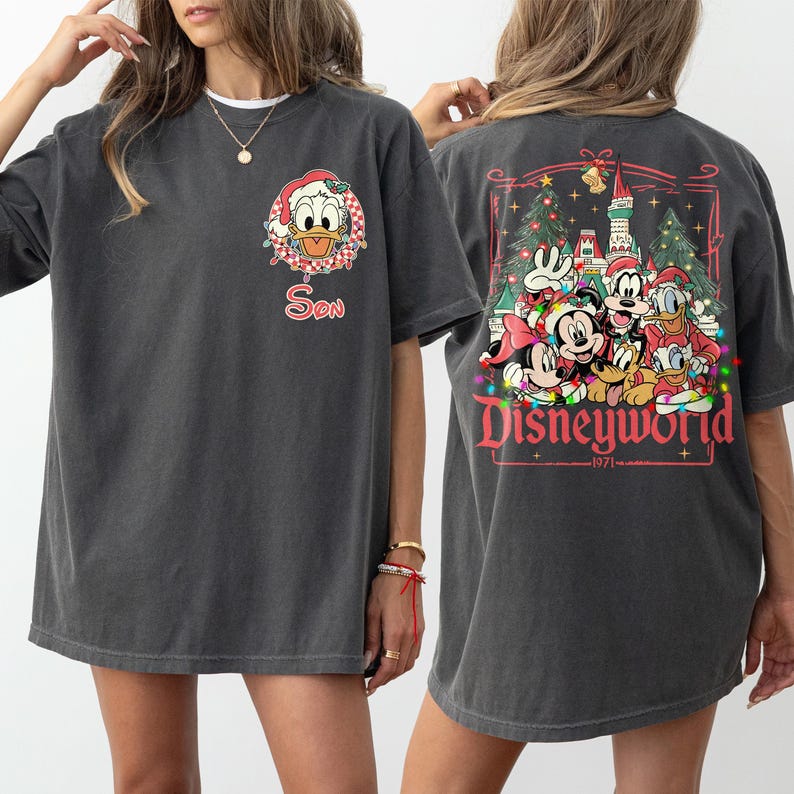 May include: Dark gray t-shirt featuring a front graphic of Donald Duck in a Santa hat with the word "Son". The back of the shirt displays a Disneyworld graphic with Mickey and Minnie Mouse, Goofy, Donald Duck, and Pluto.