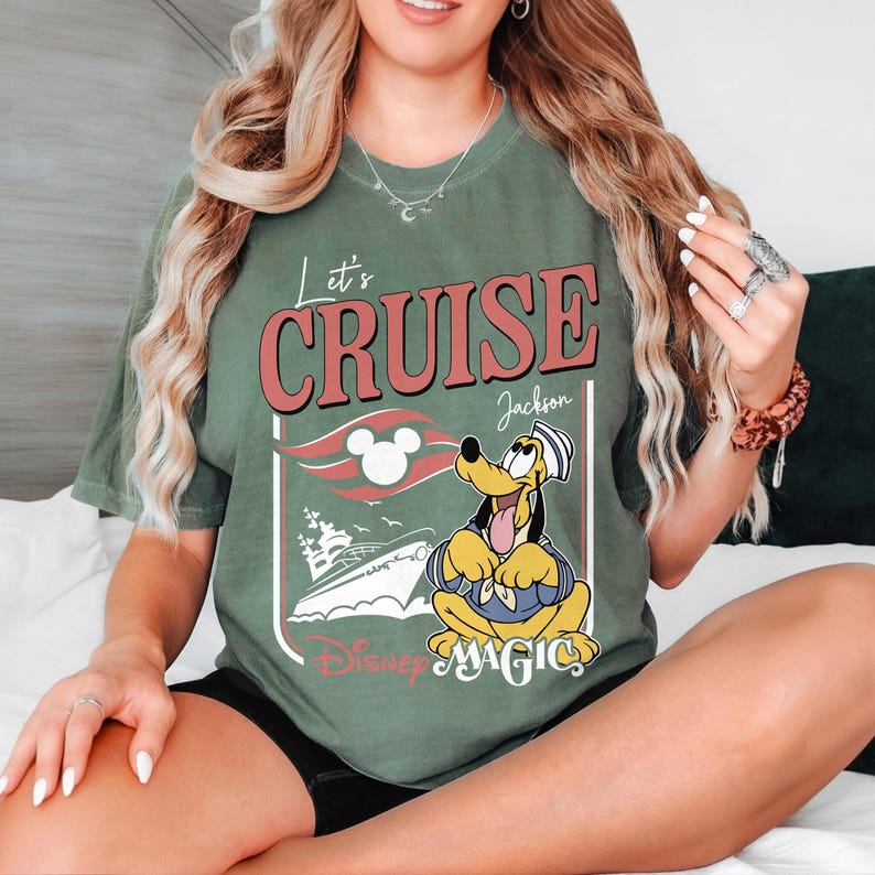 May include: Olive green t-shirt with the words "Let's Cruise" in red and white. The shirt features a cartoon of Pluto in a sailor outfit, a cruise ship, and the words "Disney Magic".