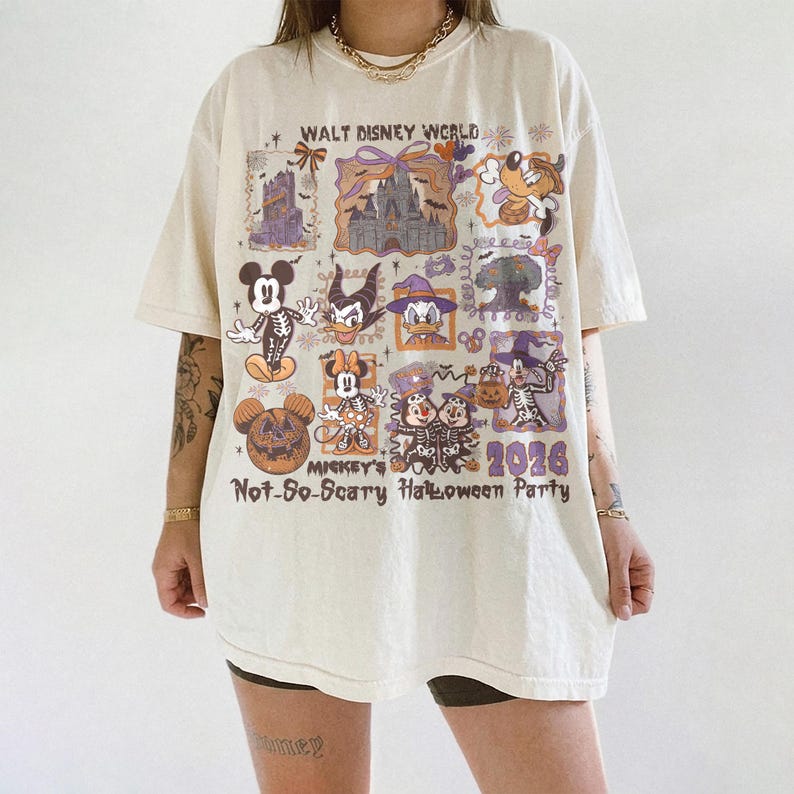 May include: Cream-colored t-shirt featuring a colorful graphic design with Disney characters in Halloween costumes. The shirt includes the text "Walt Disney World" and "Mickey's Not-So-Scary Halloween Party 2026".