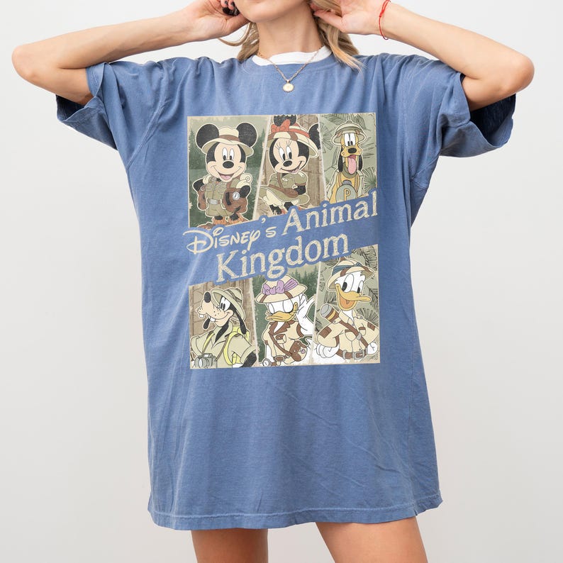 May include: Blue t-shirt featuring a graphic of Disney characters in safari outfits. The graphic includes Mickey Mouse, Minnie Mouse, Goofy, Donald Duck, and Daisy Duck, with the text "Disney's Animal Kingdom".